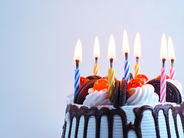 Primer plano de velas iluminadas en el pastel contra un fondo blanco