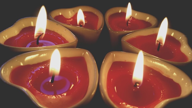 Primer plano de velas de luz de té en forma de corazón ardiendo contra un fondo negro
