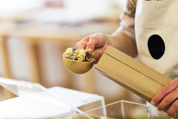 Primer plano de una vendedora tomando pasta de una bolsa de compras en una tienda orgánica.