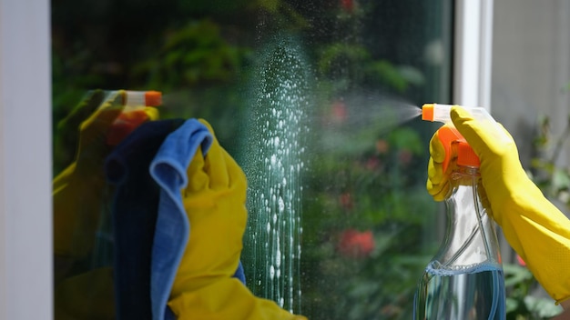 Primer plano de una ventana de limpieza limpiadora femenina con detergente y limpieza de la casa de trapo