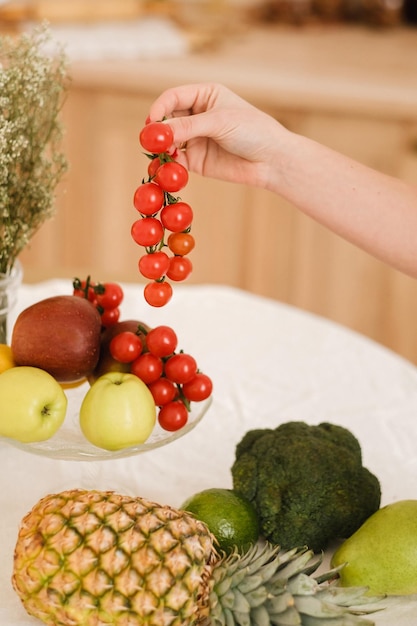 Primer plano de verduras frutas en la mesa de la cocina cocinandoLa anfitriona tiene tomates pequeños en la mano