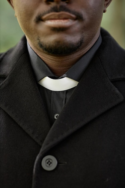 Primer plano vertical del sacerdote afroamericano vestido de negro en la ceremonia fúnebre al aire libre con enfoque en