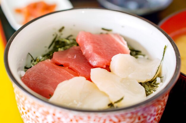 Primer plano de vieiras japonesas de marisco crudo y trozo de atún con arroz al vapor en cuenco de cerámica