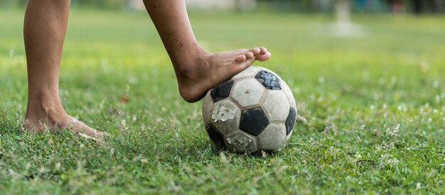 Foto un primer plano de un viejo chico de fútbol sin zapatos listo para patear la pelota en el viejo campo de fútbol