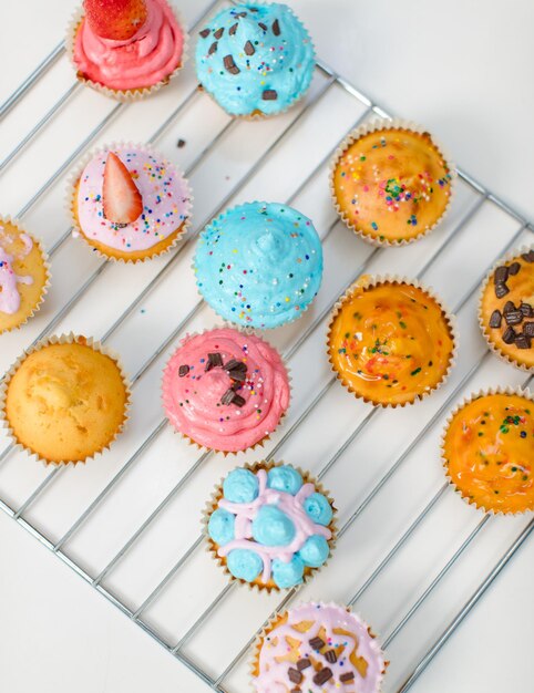 Foto en primer plano vista de arriba estudio disparado colorido receta deliciosa pasteles caseros en la parrilla de horneado decoración topping con hielo arco iris chips de chocolate galletas en rodajas frescas de fresa orgánica crema batida