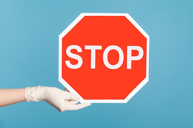 Primer plano de la vista lateral del perfil de la mano humana en guantes quirúrgicos blancos sosteniendo y mostrando la señal de Stop.