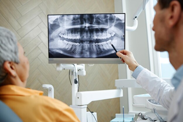 Primer plano de la vista posterior del dentista masculino apuntando a la imagen de rayos X de los dientes en la pantalla