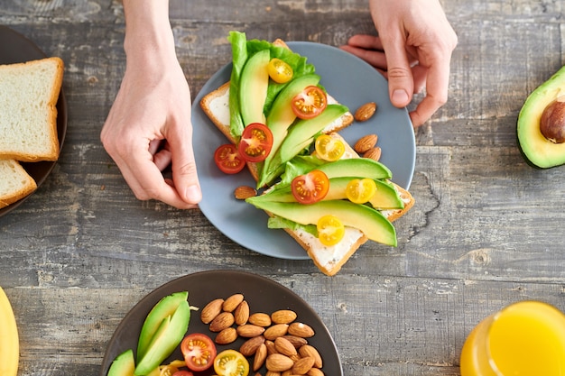 Primer plano de la vista superior de una mujer joven irreconocible haciendo sándwiches con aguacate para un desayuno saludable, espacio de copia