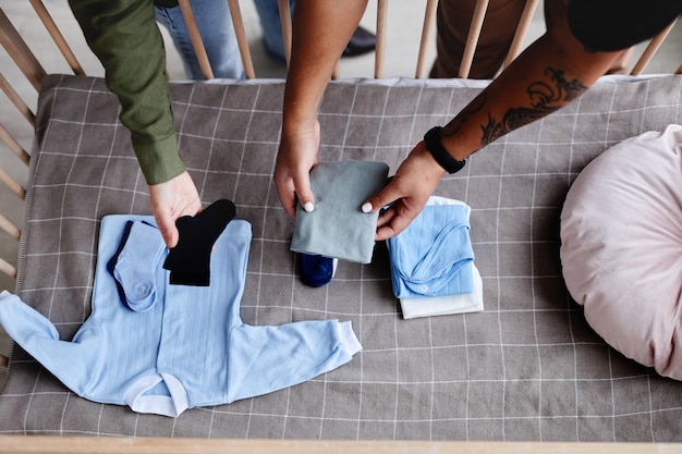 Primer plano de la vista superior de la pareja que espera un hijo y prepara la cuna con espacio de copia de ropa de bebé