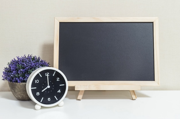 El primer reloj de alarma para decorar muestra las 8 en punto con tablero de madera negro en el escritorio de madera blanca