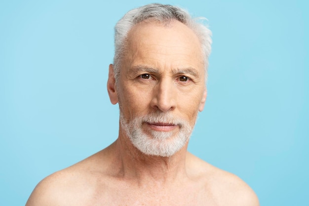 Primer retrato de un hombre mayor pensativo que se encuentran aislados sobre fondo azul Atractivo concepto masculino maduro de procedimientos de belleza para el cuidado del cuerpo
