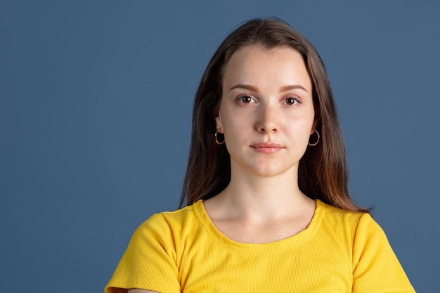 Primer retrato de una joven hermosa con camisa amarilla aislada sobre fondo azul del estudio