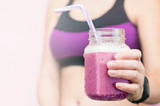 Primer de los smoothies de la baya del verano en la mano de una muchacha con un físico deportivo.