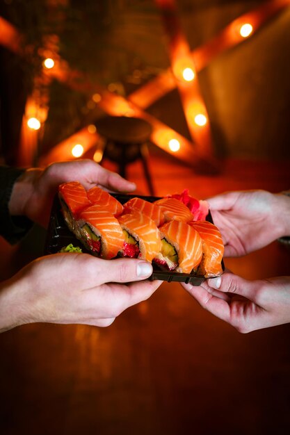 Primer sushi en caja servicio en línea de entrega de alimentos saludables. chica tiene rollos japoneses con salmón y aguacate en manos