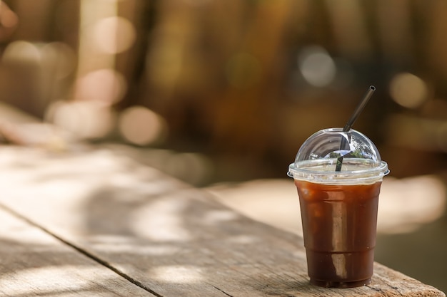 Primer de la taza plástica para llevar de café negro helado Americano en la tabla de madera con el espacio de la copia.