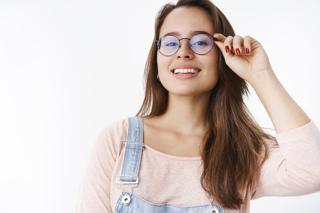 Foto primer tiro de confianza, guapa, autosatisfecha, hermosa mujer de 20 años tocando el borde de las gafas y sonriendo con orgullo