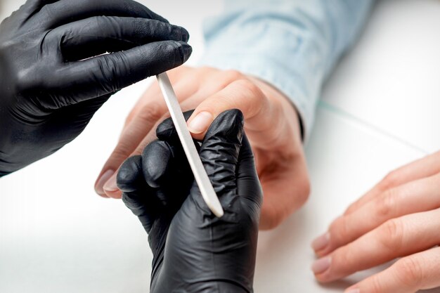 Primer tiro de mujer joven recibiendo manicura por maestro de manicura con lima de uñas en salón de uñas