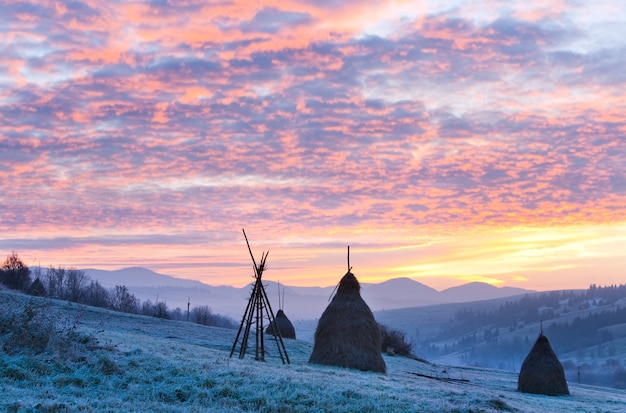 Primeras heladas de otoño en los pastos con pajares y majestuoso amanecer en la aldea de las montañas