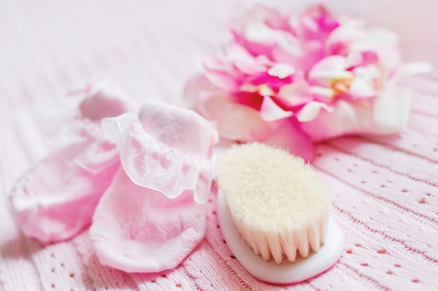 Primeros accesorios para niña recién nacida: botines rosas, gorro con flores de seda y un pequeño cepillo para el cabello.