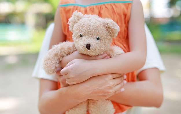 Primeros manos de niña niño y mamá abrazando oso de peluche.