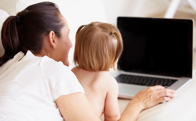 Primeros pasos en el aprendizaje Una madre y su pequeña hija miran juntas una computadora portátil