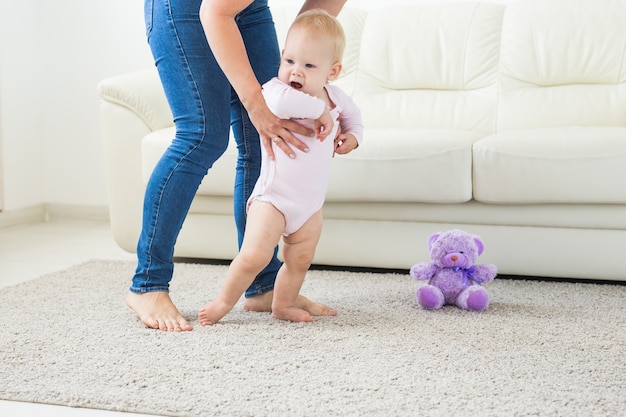 Primeros pasos de un bebé que aprende a caminar en calzado de salón blanco y soleado para niños