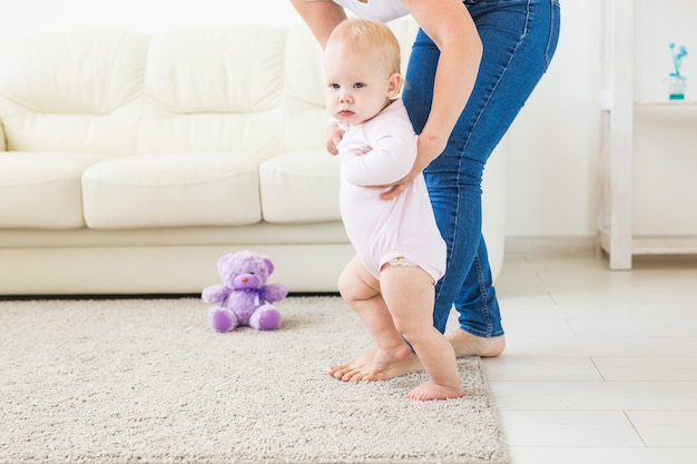 Primeros pasos de un bebé que aprende a caminar en la soleada sala de estar blanca. Calzado para niño.