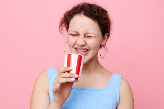 Primeros planos de una mujer alegre con un vaso desechable sobre un fondo rosa inalterado