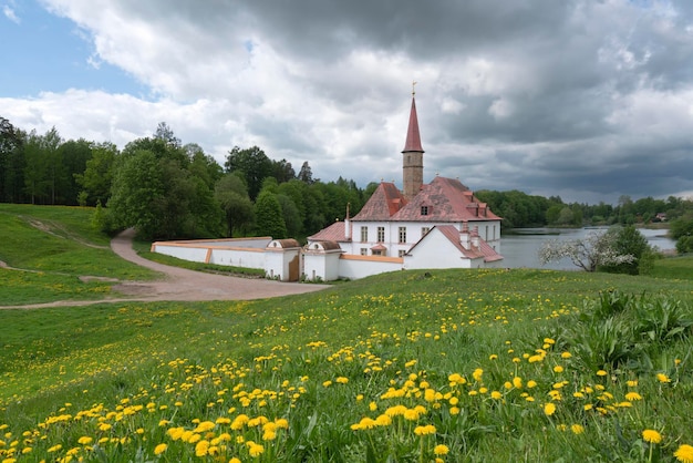 Priory Priory Palace en la orilla del Lago Negro y flores de diente de león en primer plano en un día soleado de verano Gatchina San Petersburgo Rusia