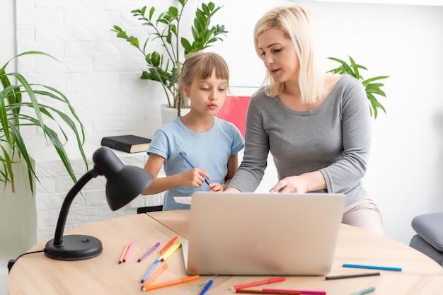 Foto privatunterricht. aufmerksame junge lehrerin hilft kleinen mädchen beim lernen der mathematischen sprache, korrigiert fehler und erklärt lernmaterial. die lächelnde mutter hilft der kleinen tochter bei der hausaufgabe.