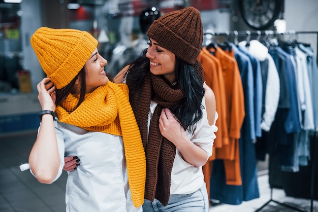 Probar gorros y bufandas abrigados. Dos mujeres jóvenes tienen un día de compras juntas en el supermercado.