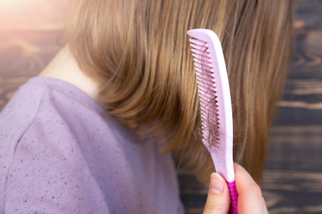 Problem mit Haarausfall. Frau hält mit rosa Kamm.