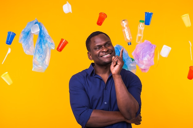 Problema de la basura, el reciclaje de plástico, la contaminación y el concepto medioambiental - Hombre afroamericano serio mirando basura en la pared amarilla. Está pensando en ecología.