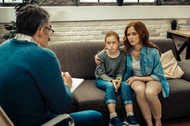 Problema de comunicação. Mulher simpática e triste abraçando a filha enquanto visitavam um psicólogo juntas