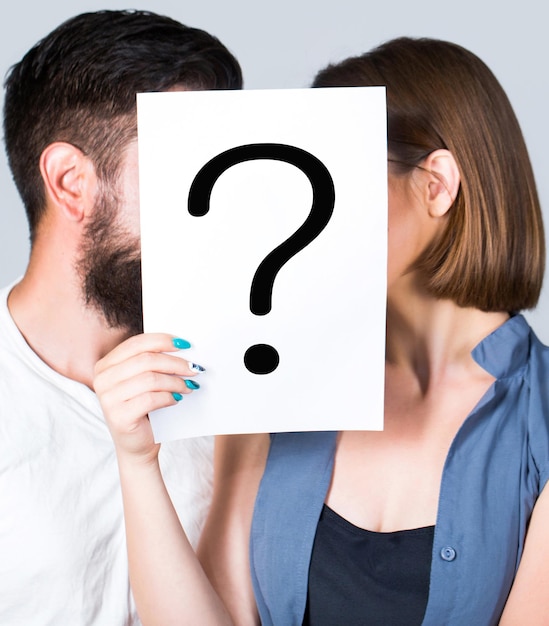 Problema en pareja, signo de interrogación. Pareja sosteniendo un signo de interrogación de papel. Pregunta anónima, hombre y mujer. Beso de pareja, incógnita. Problemas y soluciones. Pareja en pelea. Pelea entre personas.