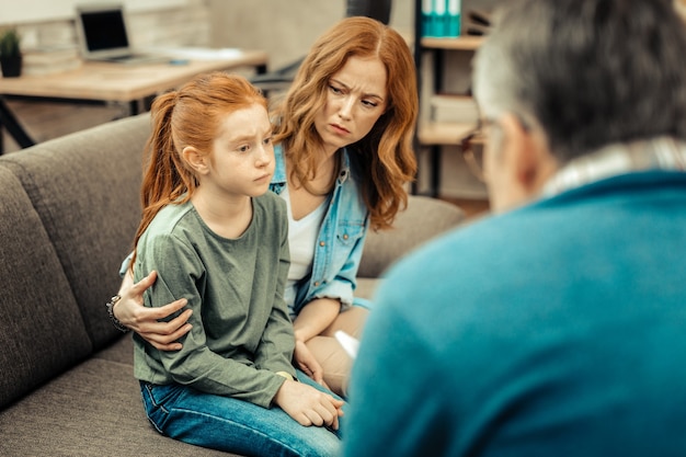 Problema psicológico. Menina simpática e triste sentada no sofá enquanto sofre de autismo