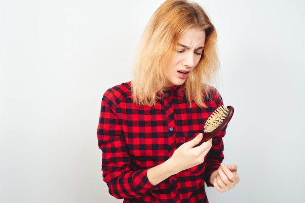 Problemas con el cabello. Chica con cepillo sobre fondo blanco en la camisa roja