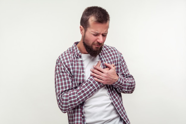 Problemas cardiológicos de ataque cardíaco Retrato de homem barbudo estressado na camisa xadrez, agarrando o peito, sofrendo de dor aguda, cãibra risco de infarto, tiro de estúdio interno isolado no fundo branco