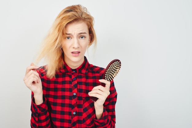 Problemas com o cabelo. Menina com escova de cabelo no fundo branco na camisa vermelha