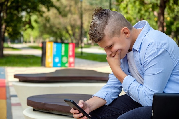 Problemas das crianças modernas. Cara jovem no parque com o telefone chateado