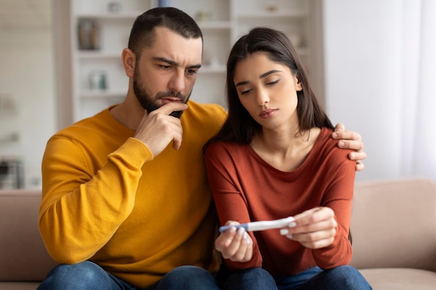 Problemas de infertilidade retrato de um jovem casal chateado olhando para um teste de gravidez negativo