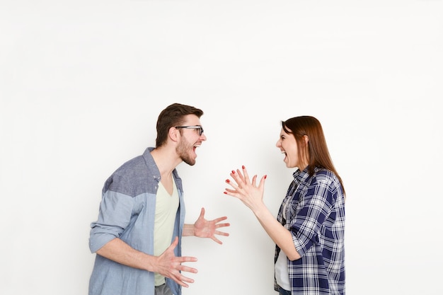 Problemas de relacionamento. Jovem casal discutindo, gritando um com o outro por causa de desentendimentos, isolado no branco