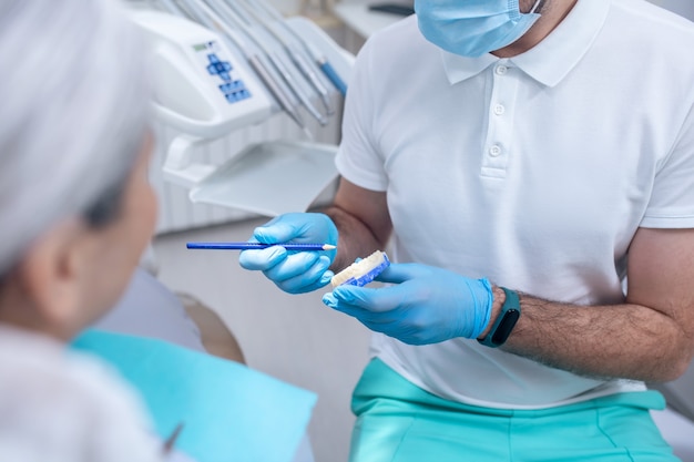 Problemas dentales. Joven dentista mostrando una dentadura a su paciente