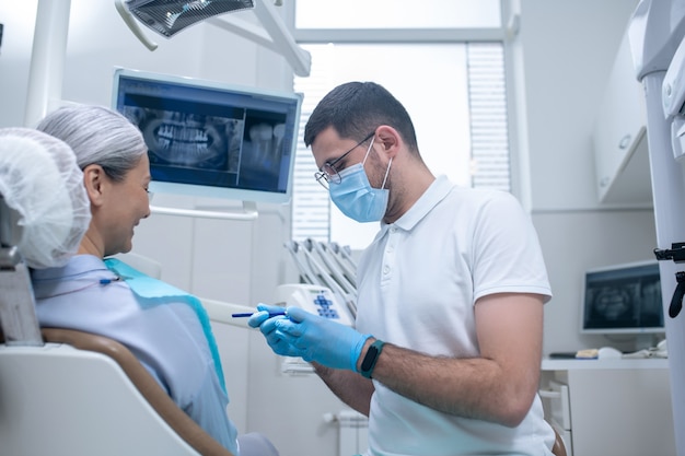 Problemas dentários. Jovem dentista mostrando uma dentadura para sua paciente