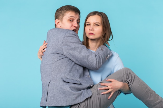 Problemas familiares, responsabilidade, feminismo e conceito de relacionamento - mulher carregando o homem nos braços sobre fundo azul.