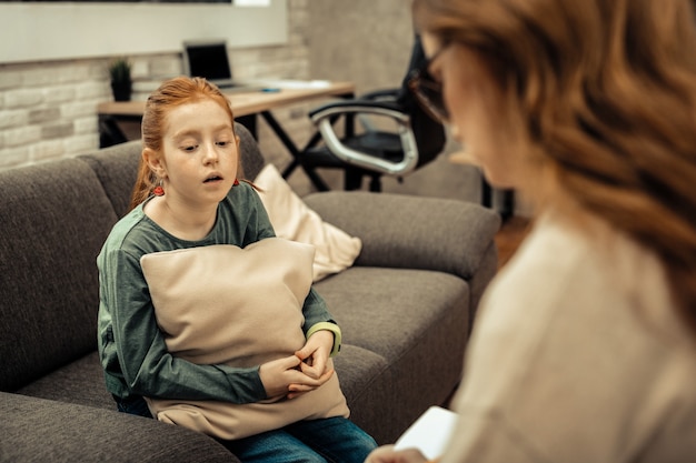 Problemas de la infancia. Triste niña triste hablando sobre sus dificultades en la vida mientras tiene una sesión con un psicólogo