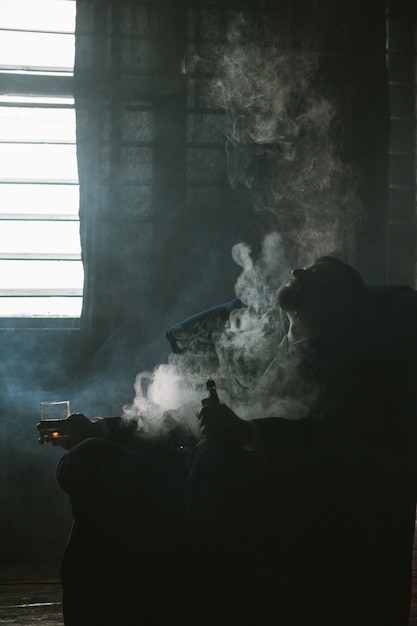 Foto problemas masculinos en la vida. accidente de carrera. el hombre exitoso lo perdió todo, la desesperación por el alcohol y el vapeo. cansado en quiebra, chico irreconocible en el humo, el fondo del cuarto oscuro, el concepto de quiebra