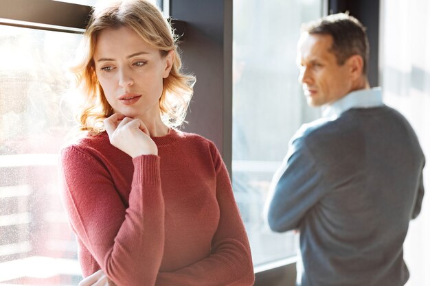 Problemas en las relaciones. Triste infeliz mujer triste de pie cerca de su novio y sosteniendo su barbilla mientras se siente deprimida