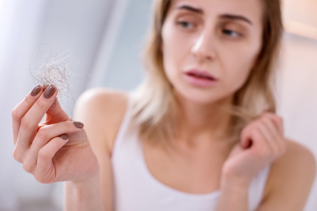 Problemas de salud. Triste infeliz mujer mirando su cabello mientras sufre de una enfermedad