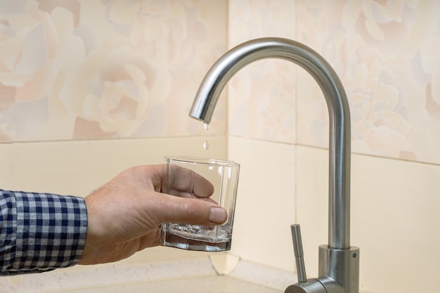 Problemas con el suministro de agua en el apartamento El grifo gotea con las gotas de agua en un vaso Concepto de crisis de agua